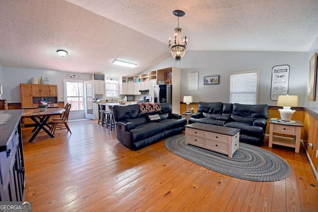 living room with light wood finished floors, an inviting chandelier, a textured ceiling, and lofted ceiling