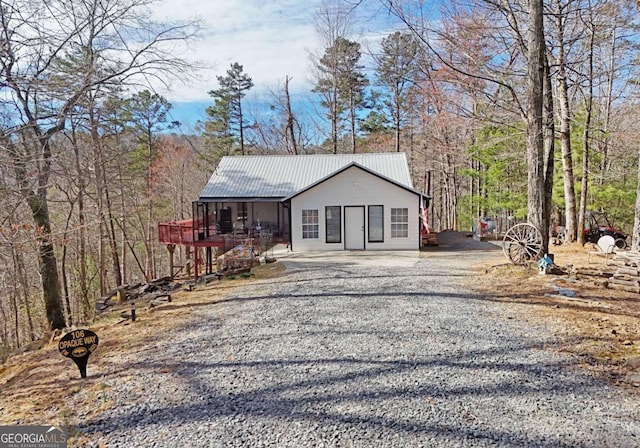 view of front facade with gravel driveway, a view of trees, and metal roof