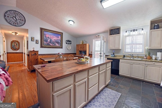 kitchen featuring a sink, black dishwasher, wainscoting, butcher block counters, and lofted ceiling