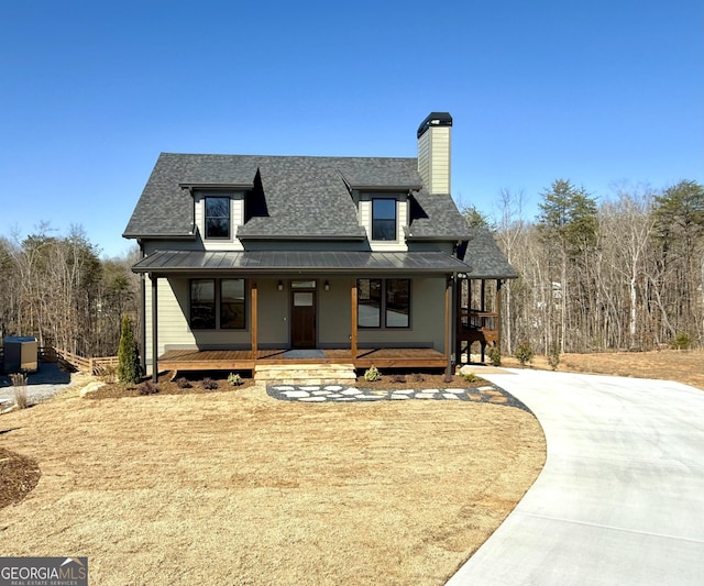 view of front of house featuring a standing seam roof, a porch, roof with shingles, metal roof, and a chimney