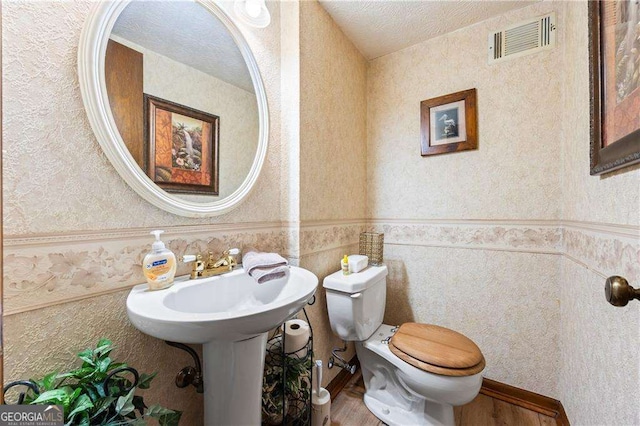 bathroom with visible vents, toilet, wainscoting, wood finished floors, and a textured ceiling