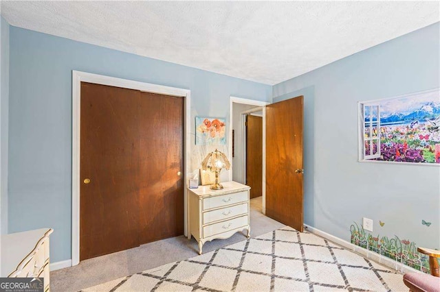 bedroom with a closet, baseboards, light colored carpet, and a textured ceiling