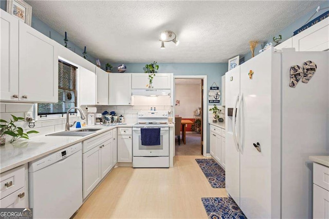 kitchen with white appliances, a sink, decorative backsplash, light countertops, and under cabinet range hood