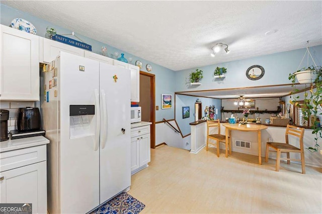 kitchen featuring white appliances, visible vents, light countertops, a textured ceiling, and white cabinetry