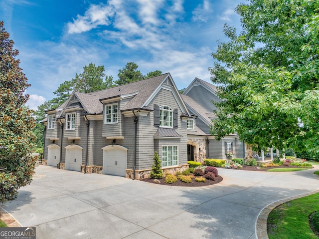 view of front of house with a standing seam roof, a garage, driveway, stone siding, and roof with shingles
