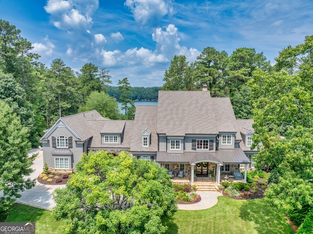 view of front of home with a standing seam roof, a front yard, metal roof, covered porch, and stone siding