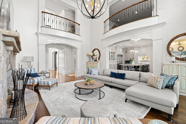 living room with a towering ceiling, a chandelier, wood finished floors, and arched walkways