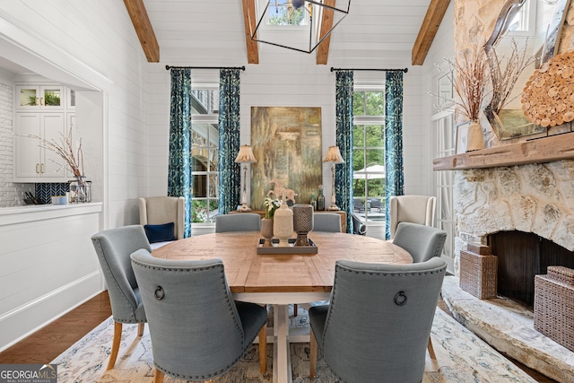 dining space with wooden walls, vaulted ceiling with beams, wood finished floors, and a stone fireplace