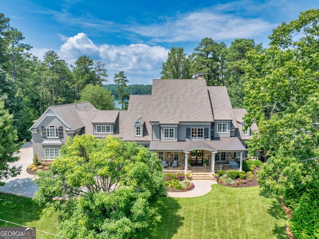 view of front of home with a chimney, a porch, a standing seam roof, stone siding, and a front lawn