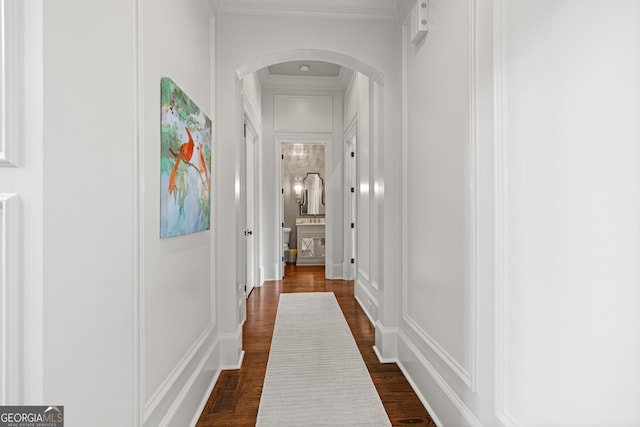 hall with arched walkways, crown molding, dark wood-type flooring, and a decorative wall