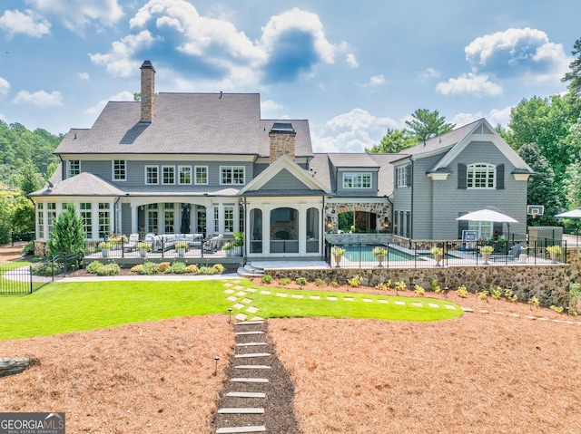 rear view of property with a patio, a fenced in pool, a chimney, fence, and a yard