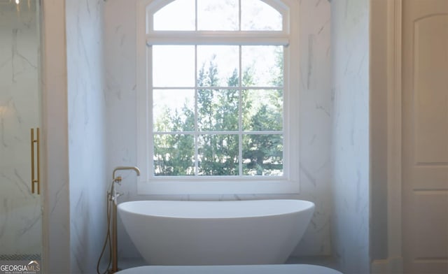 bathroom featuring a marble finish shower and a freestanding tub