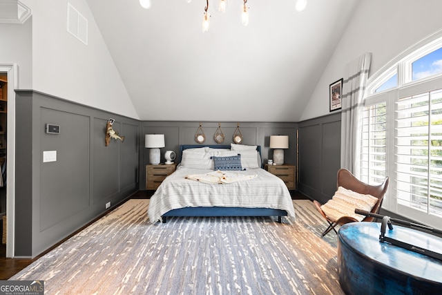 bedroom featuring visible vents, wood finished floors, a decorative wall, and high vaulted ceiling
