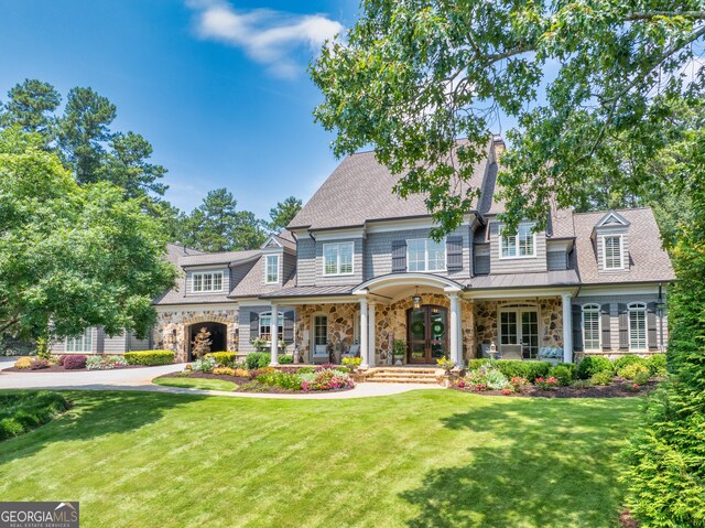 view of front of home featuring a porch, a front lawn, a standing seam roof, a shingled roof, and stone siding