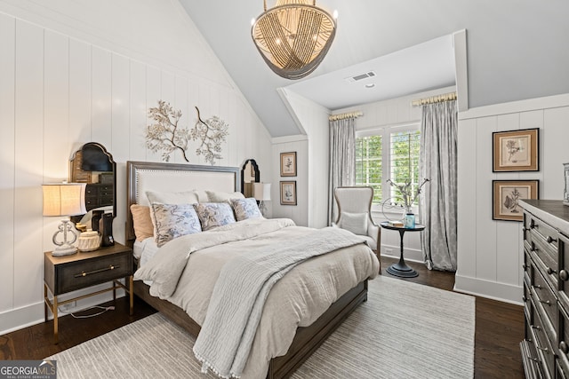 bedroom with an inviting chandelier, dark wood-style flooring, visible vents, a decorative wall, and lofted ceiling