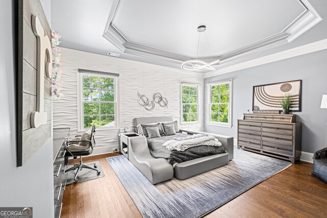 bedroom featuring wood finished floors, a raised ceiling, ornamental molding, and multiple windows