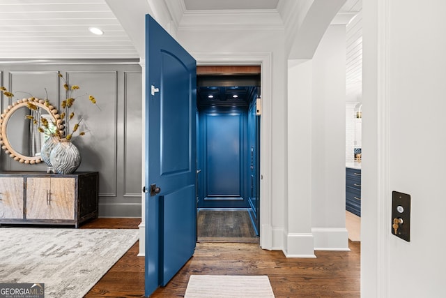 hall featuring dark wood-style flooring, a decorative wall, baseboards, ornamental molding, and arched walkways