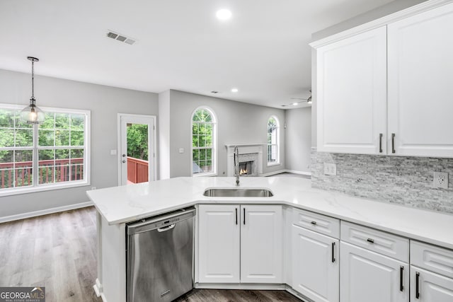 kitchen featuring visible vents, a peninsula, a warm lit fireplace, dishwasher, and tasteful backsplash