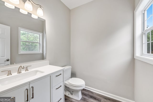 half bath with vanity, wood finished floors, toilet, and a healthy amount of sunlight