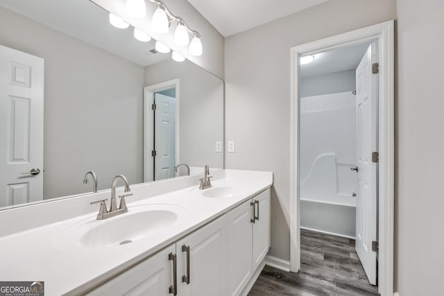 bathroom featuring double vanity, wood finished floors,  shower combination, and a sink