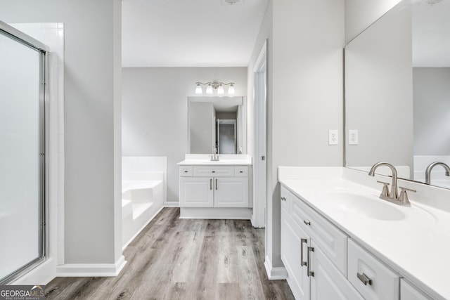 full bathroom with two vanities, a stall shower, wood finished floors, a bath, and a sink