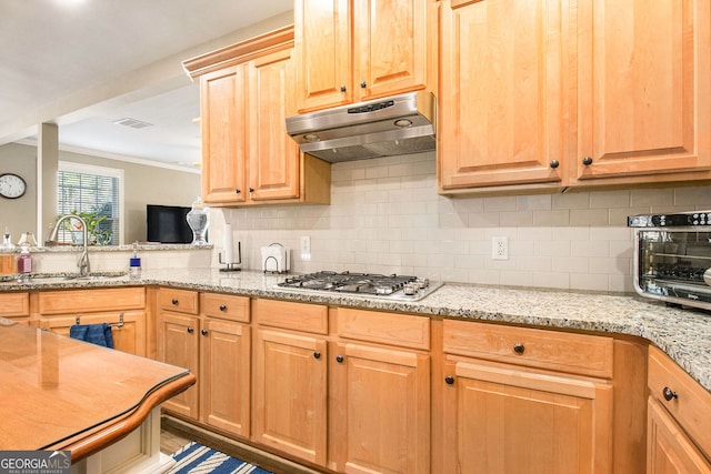 kitchen with light stone counters, a sink, decorative backsplash, stainless steel gas stovetop, and under cabinet range hood