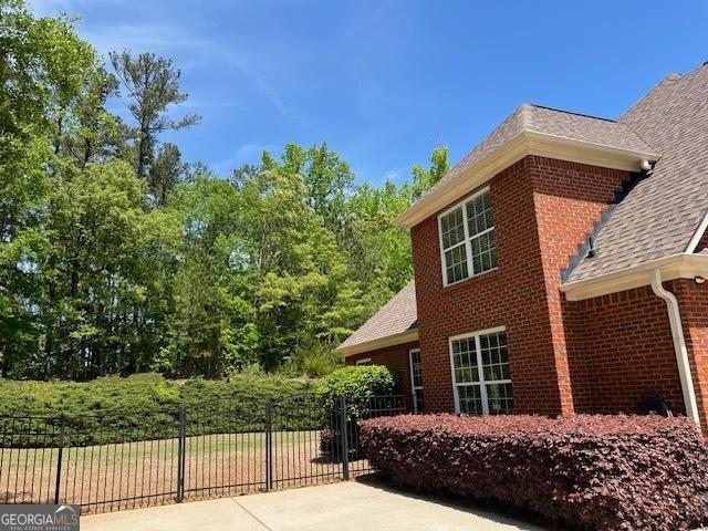 view of side of home with fence, brick siding, and roof with shingles