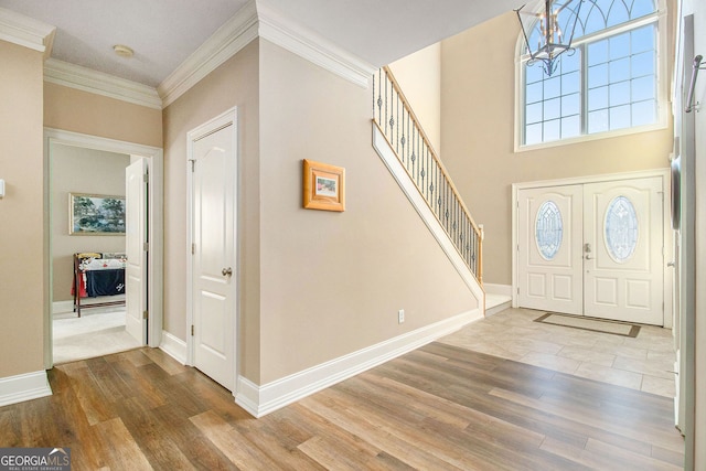 entrance foyer with baseboards, an inviting chandelier, wood finished floors, stairs, and ornamental molding