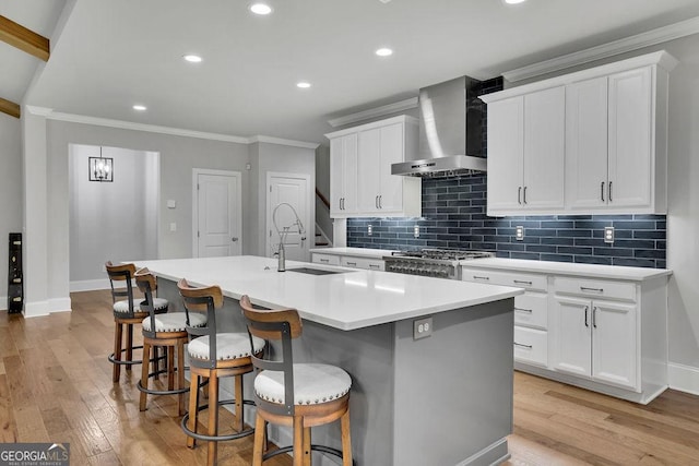 kitchen featuring a center island with sink, ornamental molding, wall chimney range hood, and range