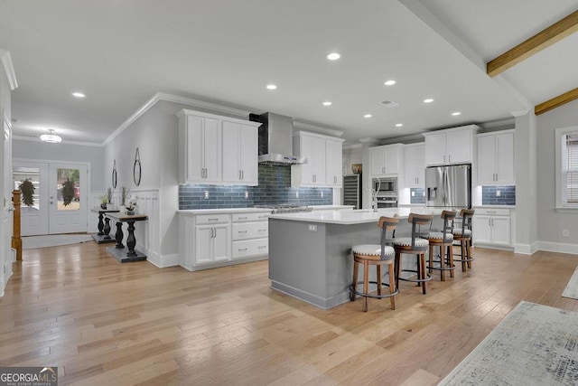 kitchen featuring wall chimney range hood, a kitchen breakfast bar, stainless steel appliances, french doors, and light wood finished floors