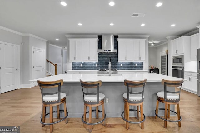 kitchen with light wood-type flooring, visible vents, a large island, appliances with stainless steel finishes, and wall chimney range hood