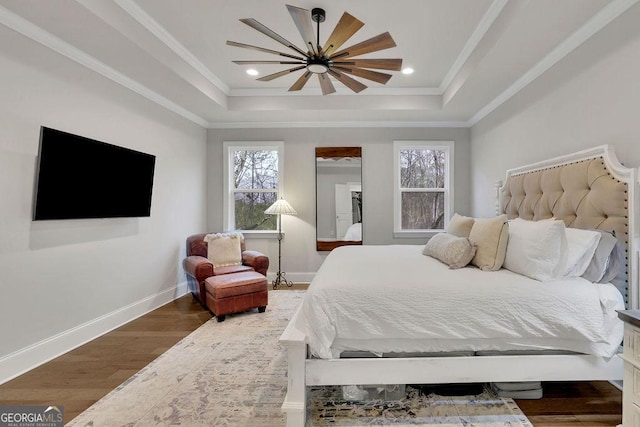 bedroom featuring wood finished floors, a raised ceiling, and ornamental molding