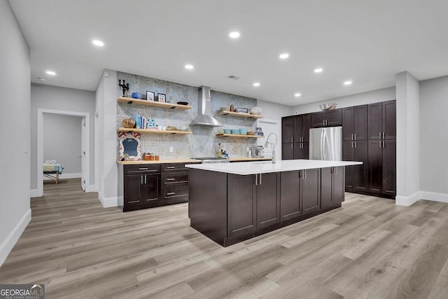 kitchen featuring light countertops, decorative backsplash, stainless steel refrigerator, wall chimney exhaust hood, and open shelves