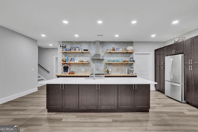 kitchen with open shelves, freestanding refrigerator, light countertops, wall chimney exhaust hood, and light wood-type flooring