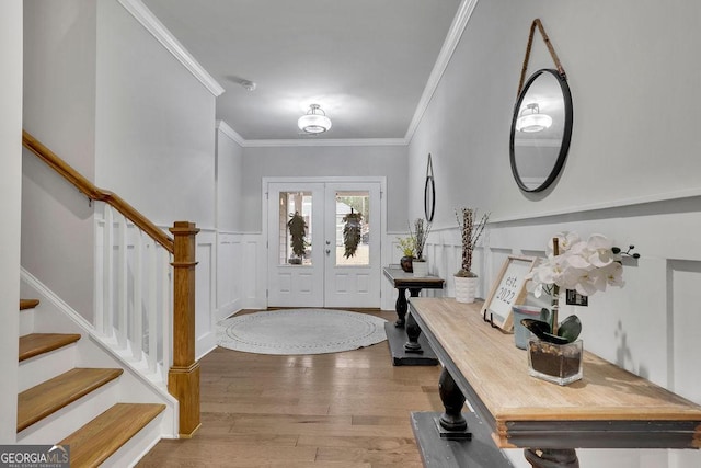 foyer entrance with a wainscoted wall, ornamental molding, wood finished floors, french doors, and stairway