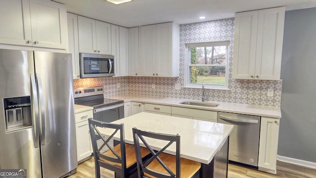 kitchen with a sink, stainless steel appliances, light countertops, white cabinets, and light wood-type flooring