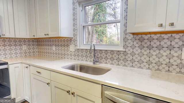 kitchen with a sink, tasteful backsplash, white cabinets, light countertops, and dishwasher