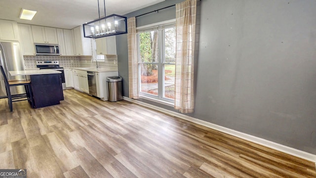 kitchen with tasteful backsplash, light wood-type flooring, light countertops, appliances with stainless steel finishes, and white cabinets