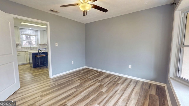 empty room featuring a ceiling fan, visible vents, baseboards, a sink, and light wood-style floors