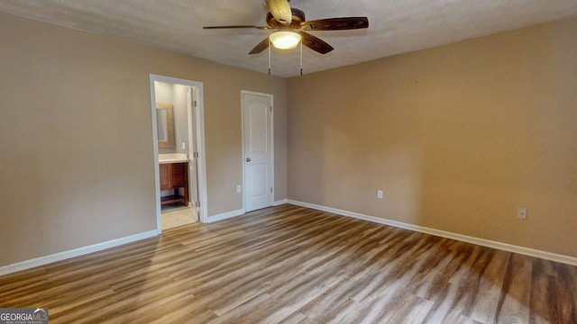 unfurnished bedroom featuring ensuite bath, ceiling fan, baseboards, and light wood-style floors