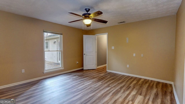 spare room featuring a ceiling fan, visible vents, wood finished floors, and baseboards