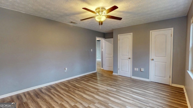 unfurnished bedroom with a textured ceiling, wood finished floors, visible vents, and baseboards