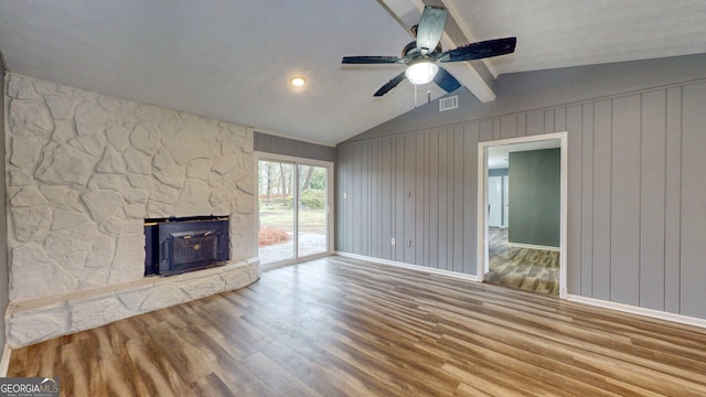 unfurnished living room featuring visible vents, wood finished floors, a stone fireplace, ceiling fan, and vaulted ceiling with beams