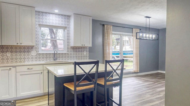 kitchen featuring baseboards, light countertops, light wood-style flooring, white cabinets, and a sink