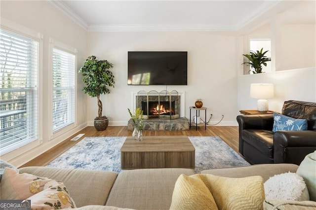 living room featuring wood finished floors, visible vents, baseboards, a warm lit fireplace, and crown molding