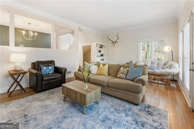 living area featuring a notable chandelier, crown molding, visible vents, and wood finished floors