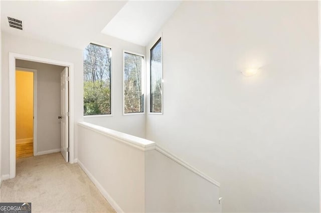 hall featuring light colored carpet, an upstairs landing, visible vents, and baseboards