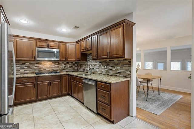 kitchen featuring light stone counters, backsplash, appliances with stainless steel finishes, and a sink