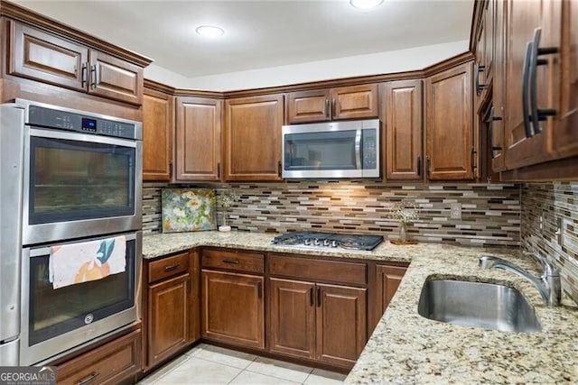 kitchen with backsplash, light stone counters, light tile patterned flooring, stainless steel appliances, and a sink