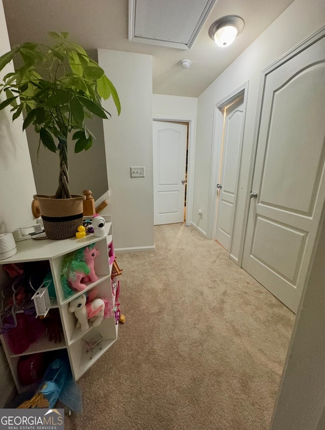hallway featuring attic access, carpet, and baseboards